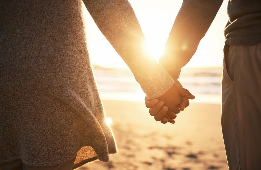 A couple holding hands and walking together towards the sunrise on a beach, a deep relationship.