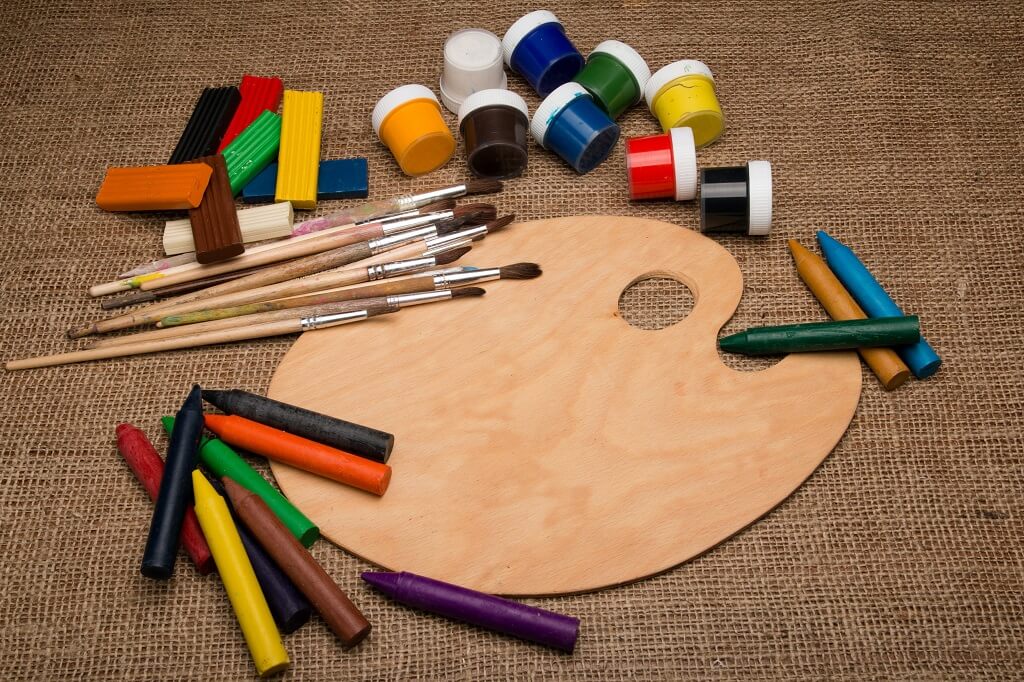 To visualize the best colors to wear to make me stronger,  the picture shows  an oval wooden painter's palette bordered by 
colored blocks, colored paints, colored crayons and paint brushes .