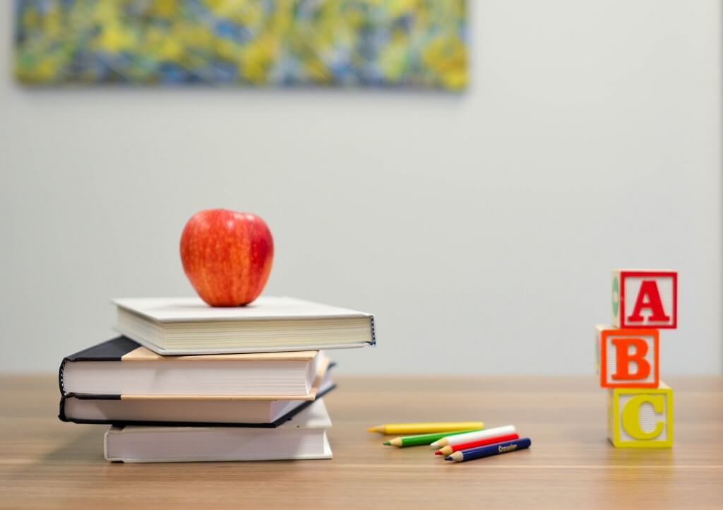 Did they teach us what the Big lie is in school? Reminding us of what we were taught at school, a picture shows us an apple, books, colored pencils and blocks on a teacher's desk.