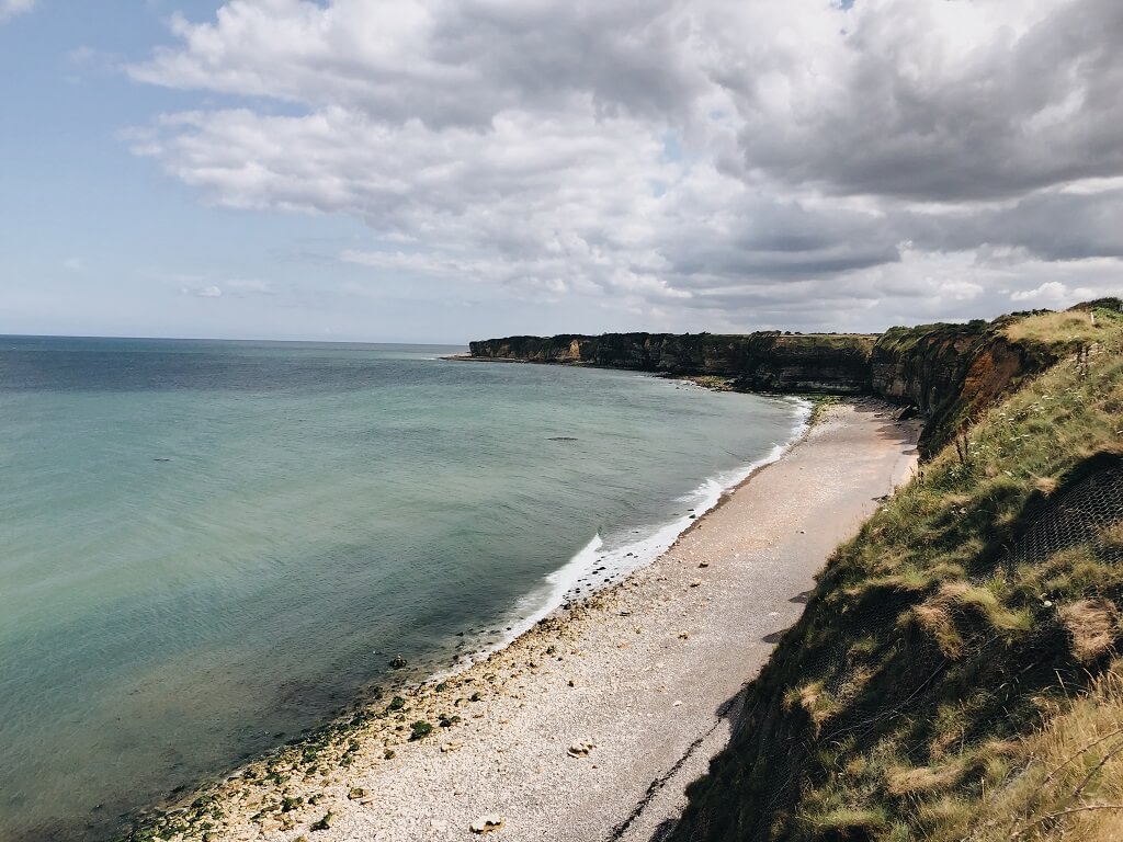 To honor the men of D Day, a photo shows the cliffs, the ocean, and a beach where the men landed.