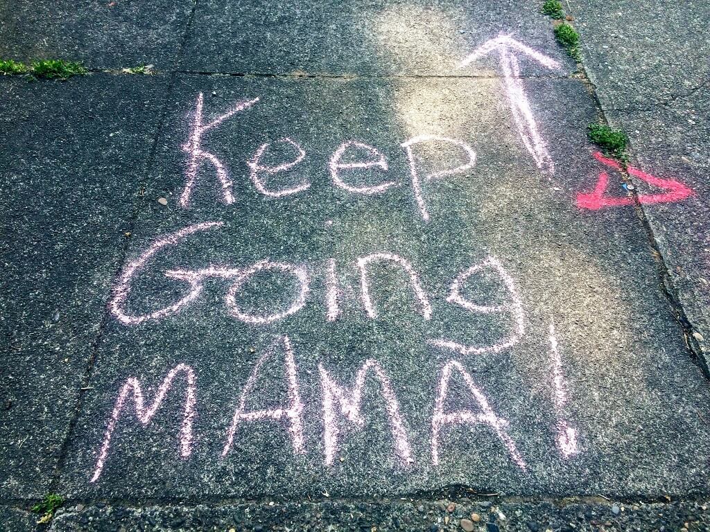 Encouragement shown in the photo. Large print written on a sidewalk says: "KEEP GOING MAMA!" with an arrow pointing forward 