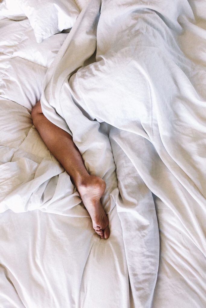Photo shows a person with a problem lying down sleeping, mostly covered by a white blanket.