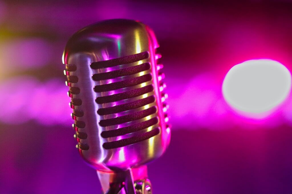 Photo shows a close up of a vintage microphone with a colorful background.  A microphone amplifies the human voice.
