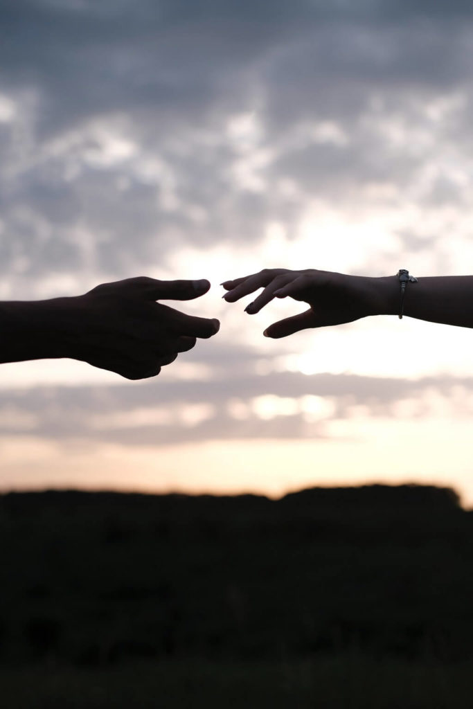 Photo shows one person’s hand and another person’s hand reaching across an ominous sky to join together in strength.