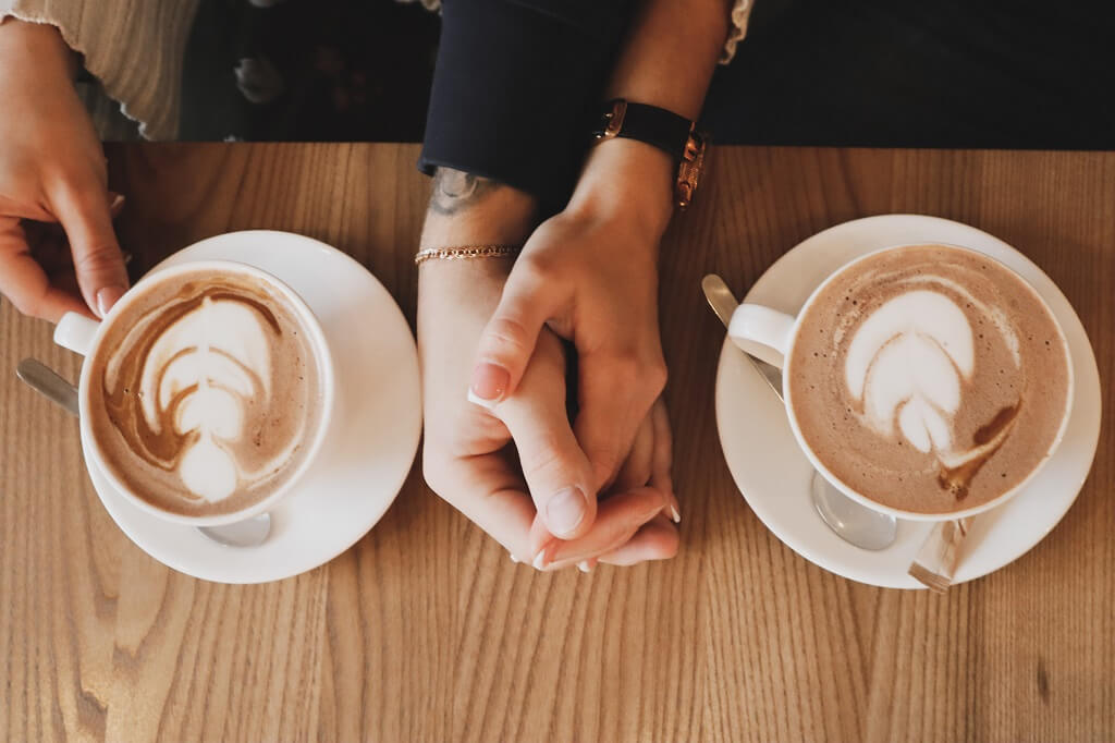 How to mingle with people is shown in this photo. The hands of two people are holding each other, 
resting on a table as they have coffee together.