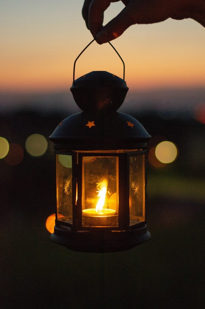 A writer can be a lamp that can give light to others. In the photo is a lit candle that glows bright golden from within a lovely lantern silhouetted against a softly colored dusk.